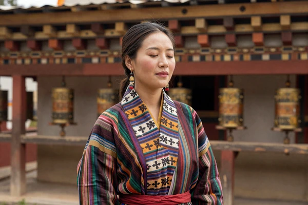 Bhutanese woman wearing traditional kira dress near Buddhist prayer wheels symbolizing cultural heritage